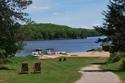 two chairs and a picnic table on a beach next to a lake at Trillium Resort & Spa in Port Sydney