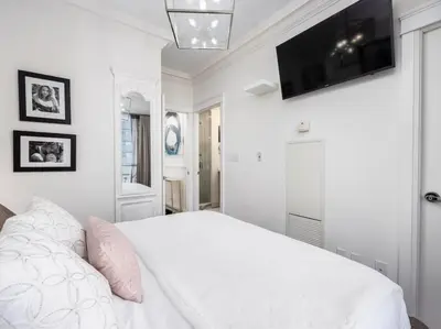 a white bedroom with a bed and a flat screen tv at Pristine Modern 2BR Condo Private BBQ and Balcony in Toronto