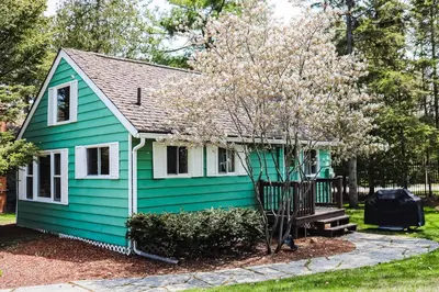 a green house with a tree in front of it at Fiddlers Green Cottage Two in Wasaga Beach