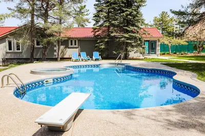 a swimming pool with blue chairs and a house at Fiddlers Green Cottage Two in Wasaga Beach