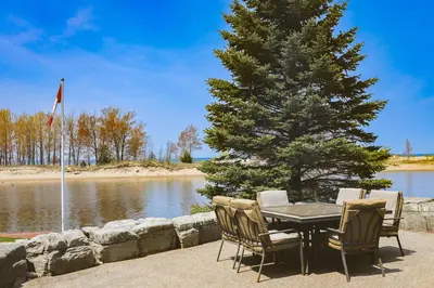 a table and chairs next to a tree and water at The Gardenhouse Cottage One in Wasaga Beach