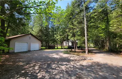 a driveway with a garage in the middle of a forest at Lovely waterfront private cottage with hot tub in Kawartha Lakes in Head Lake