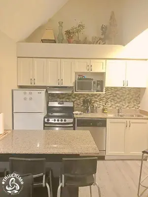 a kitchen with white cabinets and a counter with chairs at Blue Mountain, Collingwood - Loft Condo, sleeps 4 in Blue Mountains