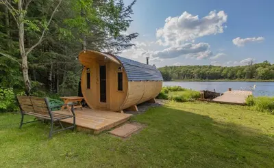 a wooden cabin with a bench next to a lake at Four Season Waterfront Muskoka Retreat in Bracebridge
