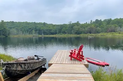 a wooden dock with a boat and a red chair on a lake at Four Season Waterfront Muskoka Retreat in Bracebridge