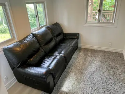 a black leather couch in a living room with two windows at Victoria Family Vacation Home - King Bed Private Yard BBQ Deck Gazebo - 4 Minutes To The Falls in Niagara Falls