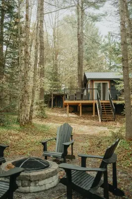 a fire pit with chairs and a cabin in the woods at The Doma Lodge - Cozy Muskoka Cabin in the Woods in Huntsville