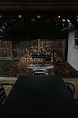 a table and chairs in a backyard with a pile of logs at The Little White Haus in Niagara on the Lake