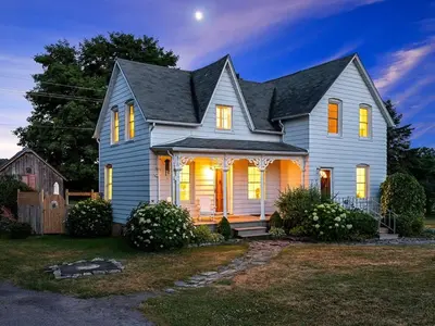 a gray house with lights on in a yard at The Gem - Beautiful farmhouse with hot tub in West Lake