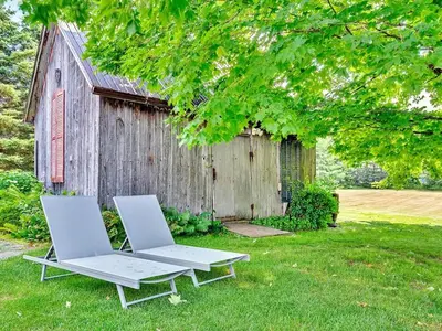two lounge chairs and a table in a yard with a barn at The Gem - Beautiful farmhouse with hot tub in West Lake