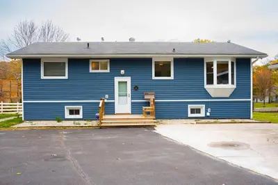 a blue house with a porch and a driveway at Riverfront Cottage Sauna Canoe Included Kids Playroom Nature Escape in Wasaga Beach