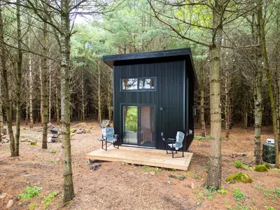 a black tiny house in the woods with two chairs at Little Cabin in the Pines in Chatsworth