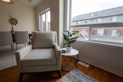 a living room with a chair and a table and a window at Townhome Steps From Lake Ontario in Hamilton