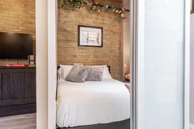 a bedroom with a white bed and a brick wall at Glyn Rhosyn Loft in Stratford
