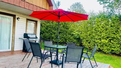 a table and chairs with a red umbrella on a patio at Charming Winter Cottage Retreat with Scenic Snow Views in Colborne