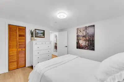 a white bedroom with a bed and a dresser at Spacious Elegance: Two Living Spaces in One Home in Burlington