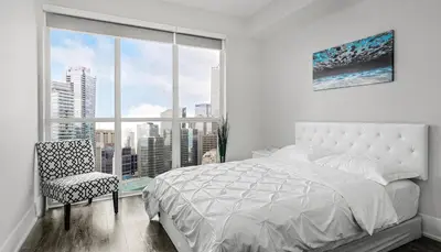a bedroom with a bed and a chair and a large window at Skyline Suites - Walk to MTCC, ACC, Rogers Centre & Entertainment District in Toronto