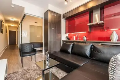 a living room with a black leather couch and red cabinets at Skyline Suites - Walk to MTCC, ACC, Rogers Centre & Entertainment District in Toronto