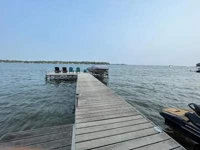 a dock with chairs and a boat on the water at Charming Cottage on Lake Simcoe in Orillia