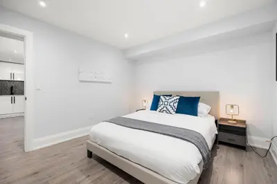 a white bedroom with a large bed with blue pillows at Cozy Modern Custom Built-Free Pkg-Game Room-Heated Floors in Toronto