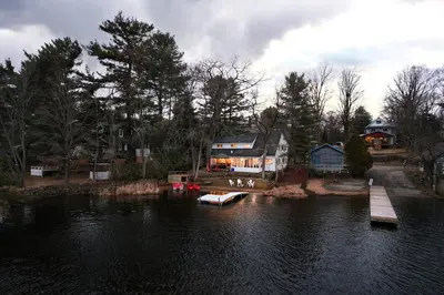 a house on a lake with a boat in the water at Muskoka Waterfront Cottage - Moon River with HOT TUB in Bala