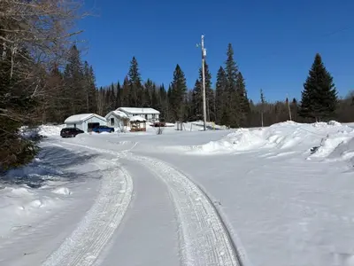 a road covered in snow with a house in the background at Peaceful and Heavenly Private Water Front Cottage on 100 Acres of Scenic Beauty- Trent Lakes in Kinmount