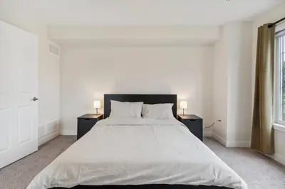 a white bedroom with a large bed with two night stands at A Brand New 4BR Townhouse in Thorold Retreat in Thorold
