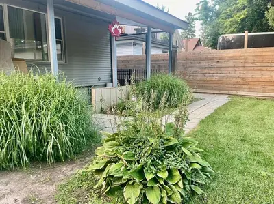 a yard with a house with a fence and plants at Stylish 3-bdrm suite w free Parking in Kitchener