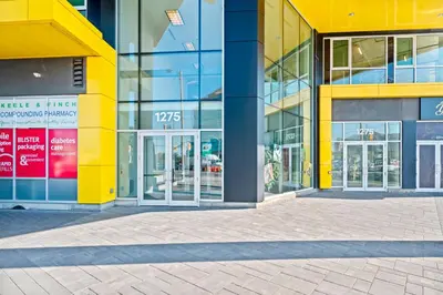 a yellow building with glass doors on a street at Finch West Residence Suites - Hotel DUKE in Toronto