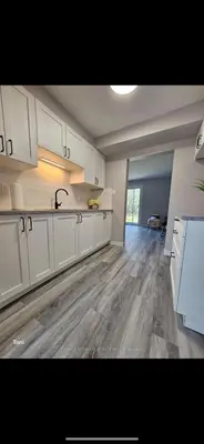 a large kitchen with white cabinets and a wooden floor at Affordable Basment Apartment - London in London