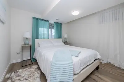 a white bedroom with a large bed with a blue blanket at Modern & Cozy 1 Bedroom with fast Wi-Fi, BBQ & Patio in Barrie