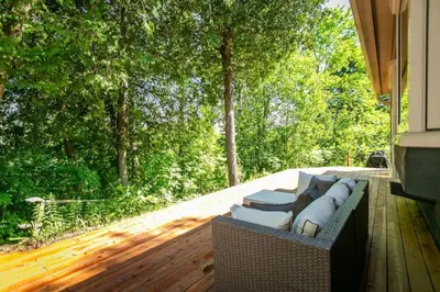 a couch sitting on a deck with trees in the background at 5BR Riverfront Retreat w Firetable BBQ and Deck in Orangeville