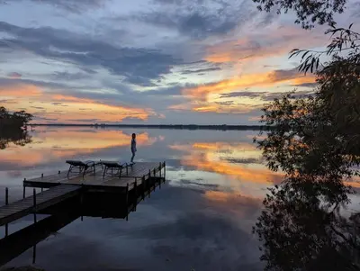 a person standing on a dock on a lake at sunset at Guest Suite w Ensuite Waterfront in Belleville