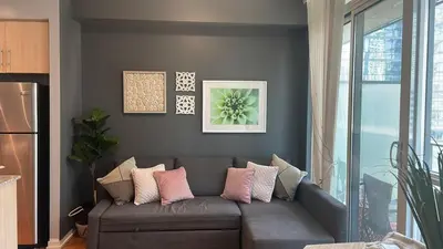 a living room with a gray couch with pink pillows at 1 BD and Den at Scotiabank Arena in Toronto