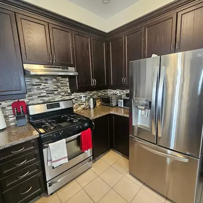 a kitchen with wooden cabinets and a stainless steel refrigerator at Exquisite Junior Bedroom in Brampton