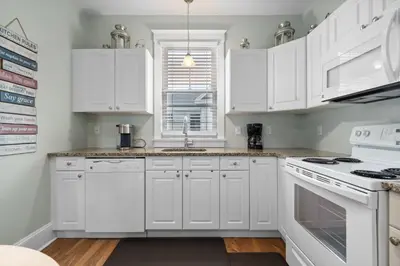 a white kitchen with white cabinets and a window at The Merlin - 61 Butternut in Cherry Valley
