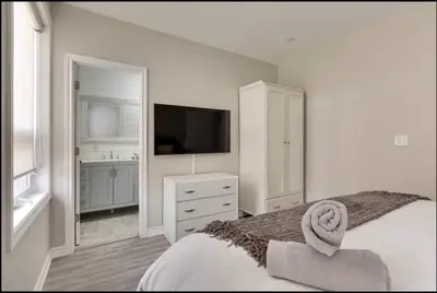 a white bedroom with a bed and a television at Casa Hotel Elegant Suite w Patio BBQ Grill in Toronto