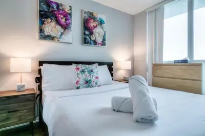 a white bedroom with two beds and two lamps at Panorama Luxe Suites - Prime Downtown Location in Toronto