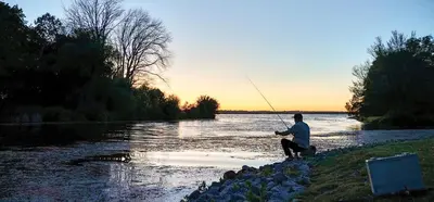 a man is fishing on a river with a dog at Scugog Landing Resort in Port Perry