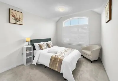 a white bedroom with a bed and a chair at Modern Comfort in Clarington in Newcastle