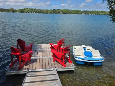 a dock with chairs and a small boat on a lake at Lovely Little Lake House in Brighton