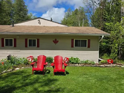 two red chairs sitting in the grass in front of a house at Lovely Little Lake House in Brighton