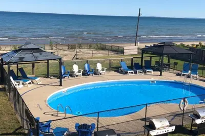 a swimming pool next to the ocean with chairs and umbrellas at The Driftwood Deck 5A in Wasaga Beach