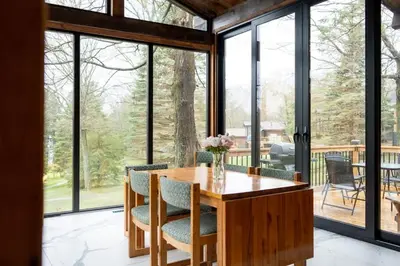 a dining room with a wooden table and chairs and large windows at Lake Muskoka Deluxe 3-bdrm Cottage - Pier 100 #80 in Port Carling