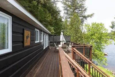 a house with a wooden deck next to the water at Muskoka Cabana - Sandy beach cottage in Muskoka in Utterson