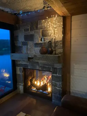 a stone fireplace in a living room with christmas lights at The Water’s Edge * * Unique Muskoka Treehouse * * in Utterson