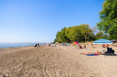 a group of people on a beach with umbrellas at Spacious Ground Floor Garden View Apartment in Wasaga Beach