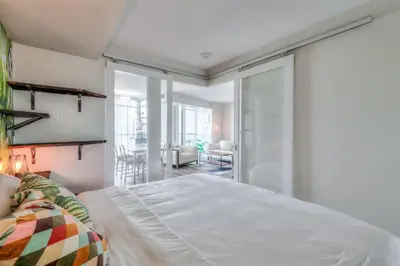 a bedroom with a white bed and a living room at Chic 1BR plus Den Condo with Fast WiFi and Free Parking in Toronto
