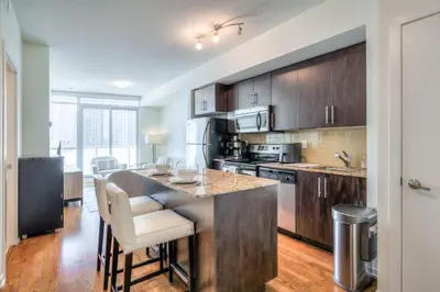 a kitchen with wooden cabinets and a kitchen island with bar chairs at 1BR plus Den Condo with Balcony in Heart of Toronto in Toronto