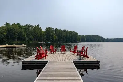 a group of red chairs sitting on a dock on a lake at Muskoka Gem 8ppfireplacescanoekayaks in Bracebridge